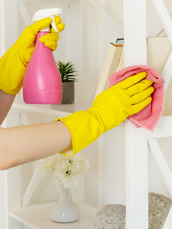 Fotografía de unas manos con guantes amarillos limpiando un mueble con producto de limpieza y trapo rosas
