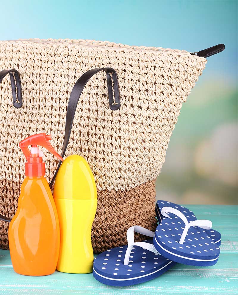 Fotografía de bolso de playa, cremas solares y chanclas