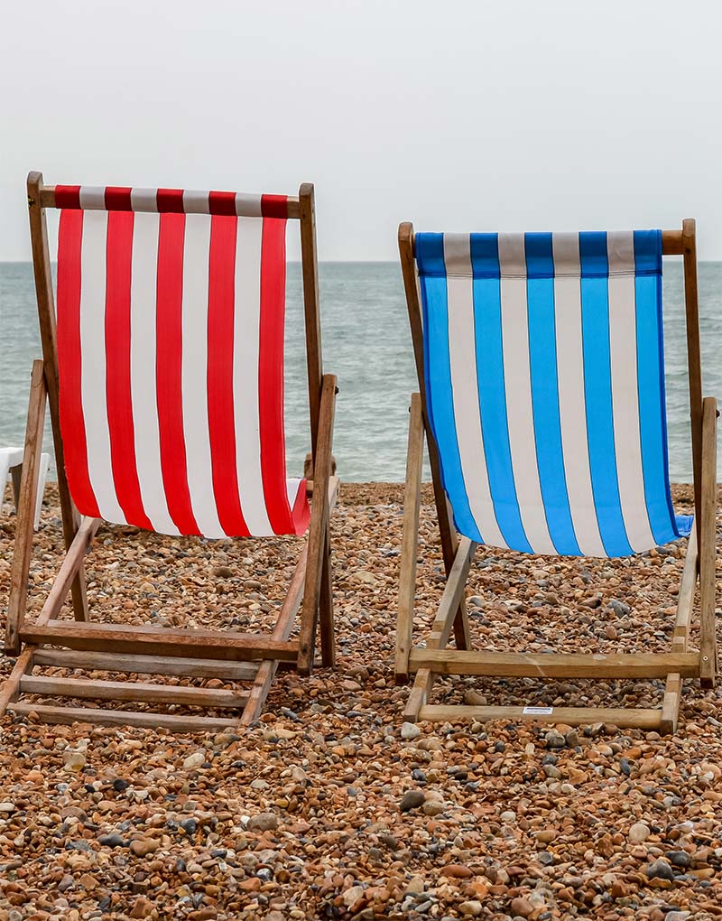 Fotografía de dos sillas de playa una roja y otra azul en la playa